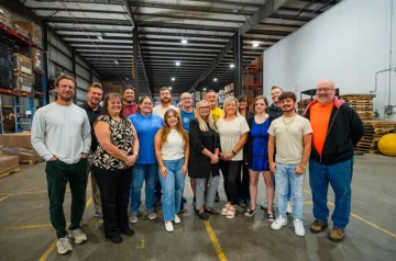 Professional foodservice wholesale distribution team posing together in industrial warehouse with pallets and logistics infrastructure visible.