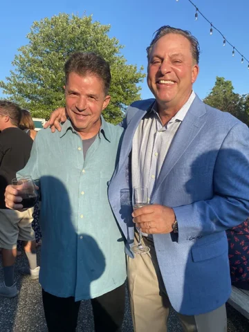 Two foodservice executives in business casual attire at an outdoor industry networking event with beverages.