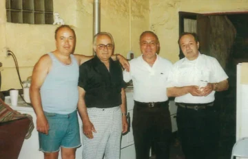 Four men in casual and business attire posing together in a 1960s commercial kitchen or warehouse facility.